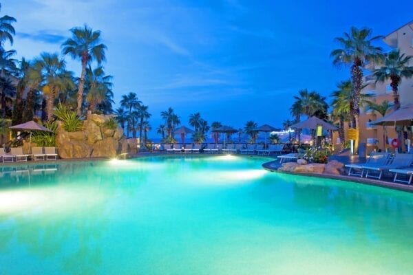 A pool with palm trees and lights in the background.